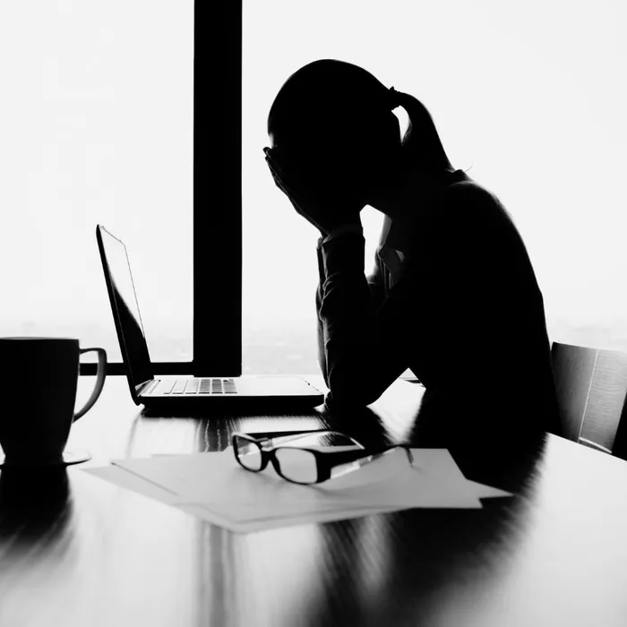 Une femme à contre-jour devant son ordinateur, la tête dans les mains