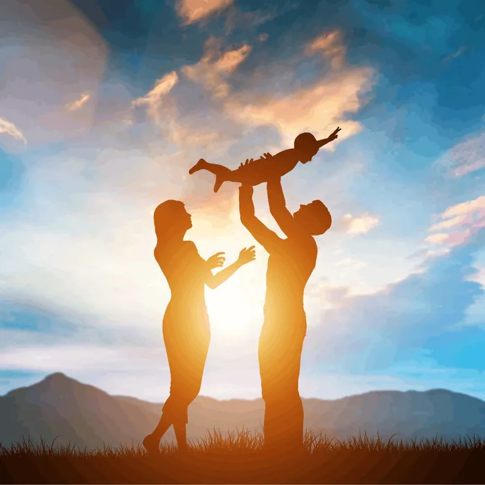 Des parents soulèvent leur enfant devant un coucher de soleil
