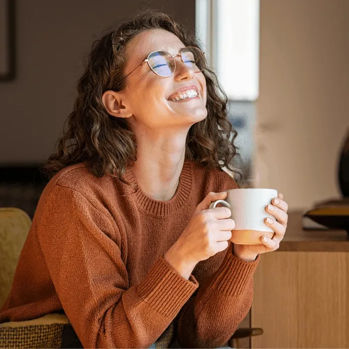 Une femme souriante tient une tasse près d'une fenêtre