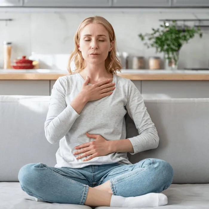 Une femme assise en tailleur, une main sur la poitrine et l'autre sur le ventre