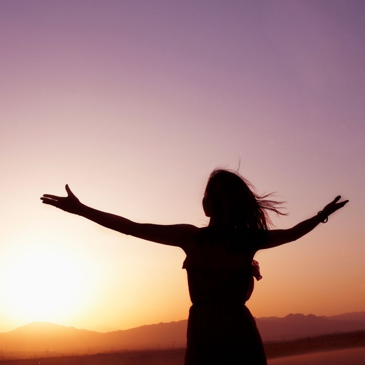 Une femme face au coucher de soleil, les bras grands ouverts