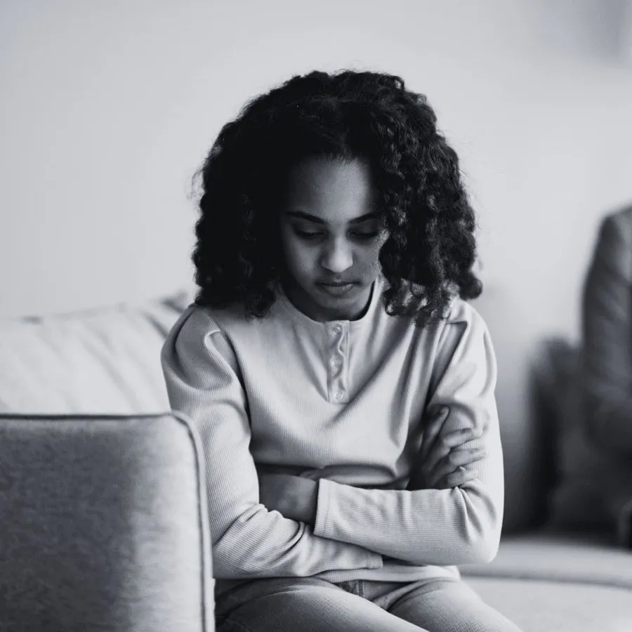 Une jeune femme assise, les bras croisés et le regard baissé